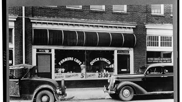 Black-and-white historical photograph showing separate signs for white and colored seating areas at a cafe restaurant.