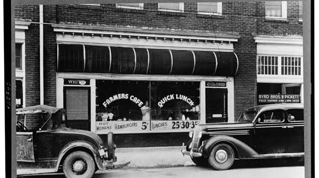 Black-and-white historical photograph showing separate signs for white and colored seating areas at a cafe restaurant.