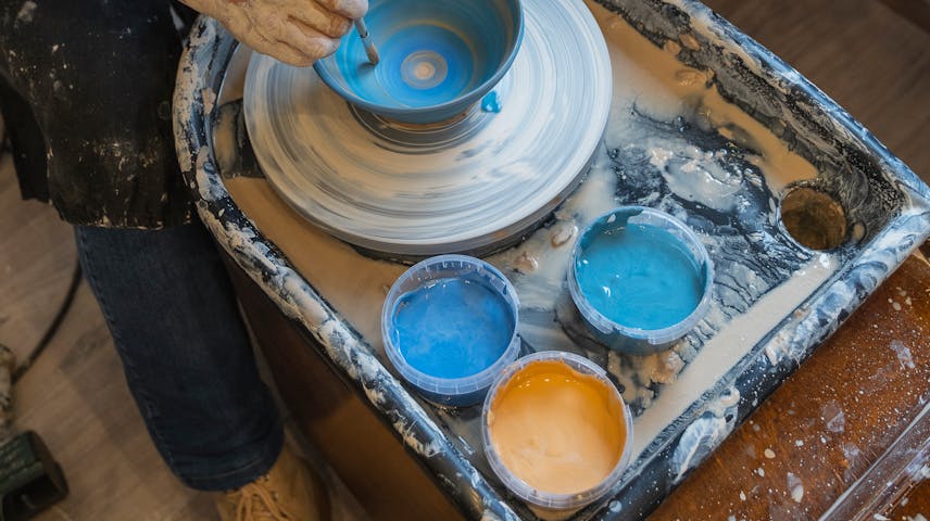 Image of a potter at a pottery wheel painting blue glaze onto a bowl.