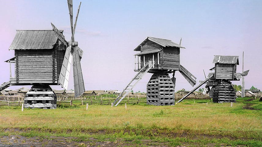 Three wooden windmills in a field.