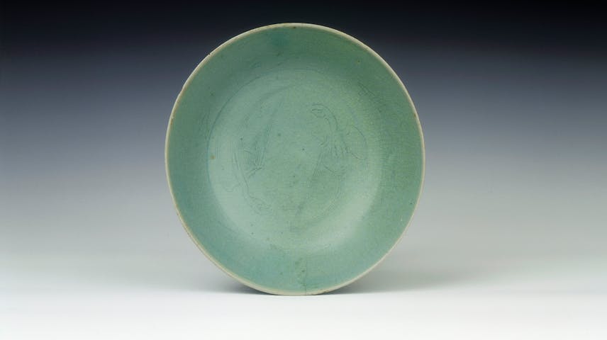 A shallow, slightly oval bowl with a bluish-green glaze and two parrot-like birds carved into it.