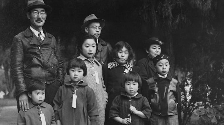 Historical black-and-white photograph of a Japanese American family waiting outdoors before removal during World War II.