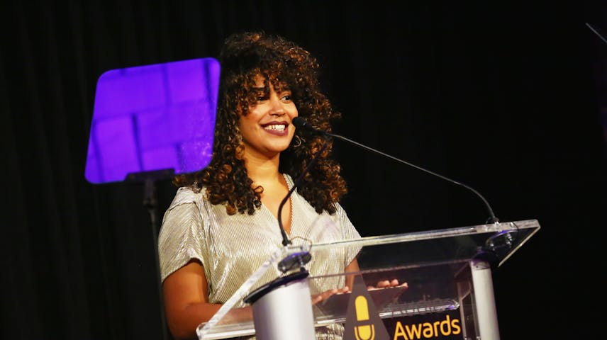 A color photograph of author Elizabeth Acevedo speaking into a microphone at a podium at an awards ceremony