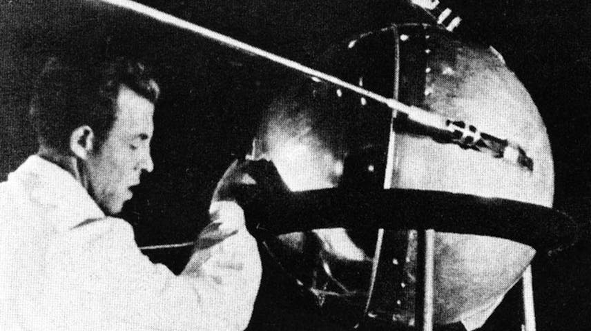 A black and white photo of a man in a lab coat working on the Sputnik satellite