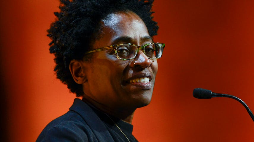 A color photograph of author Jacqueline Woodson speaking into a microphone at a podium