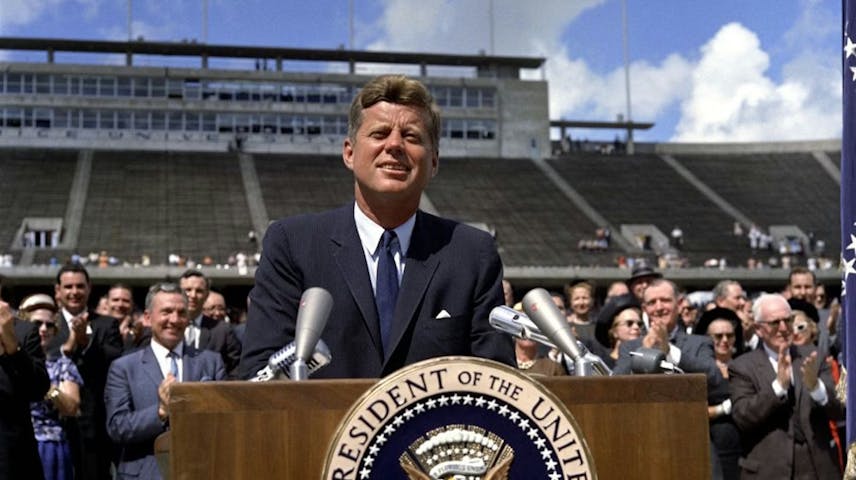 President John F. Kennedy standing at a podium outdoors in front of a large audience at Rice University.