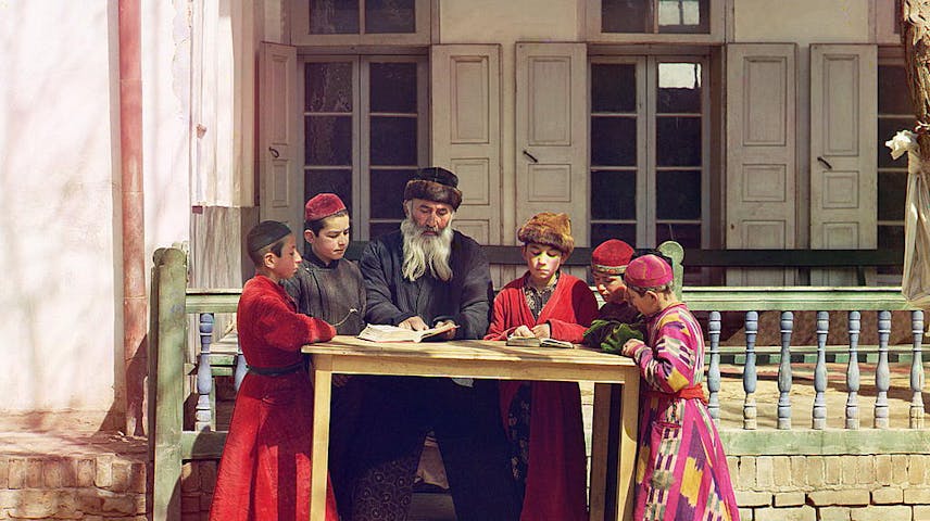A group of Jewish boys, in traditional dress, studying outside with their teacher.