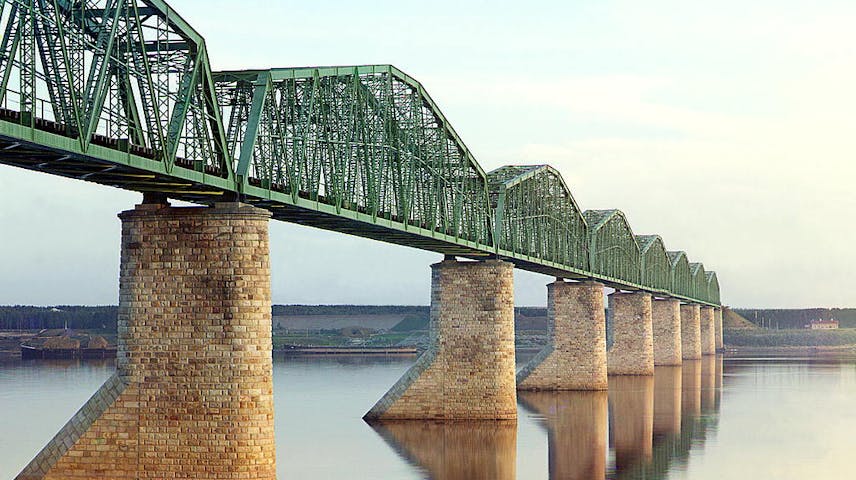 A metal truss bridge on stone piers going across a river.