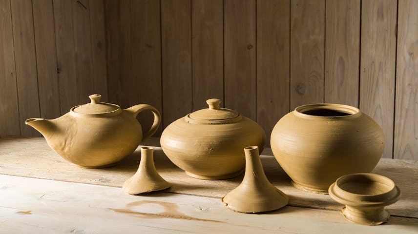 Image of a clay teapot and two small clay pots sitting on a shelf.