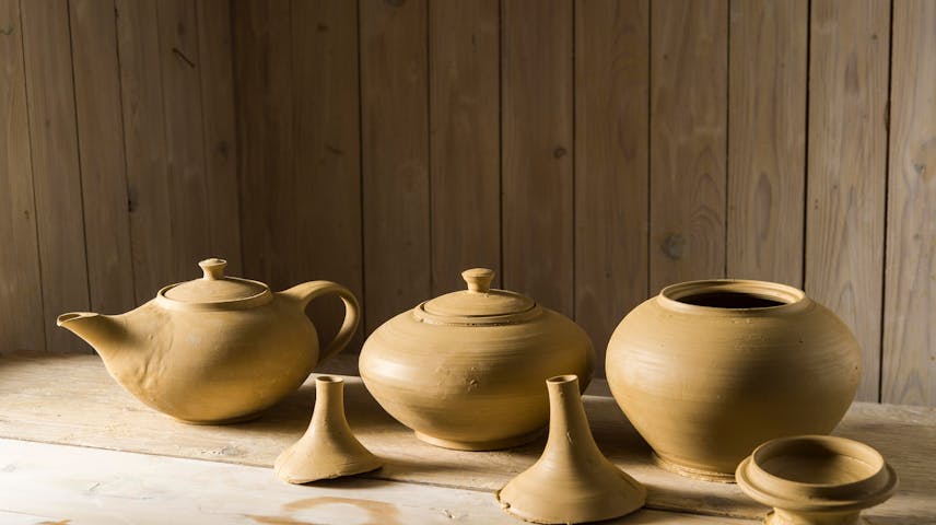 Image of a clay teapot and two small clay pots sitting on a shelf.