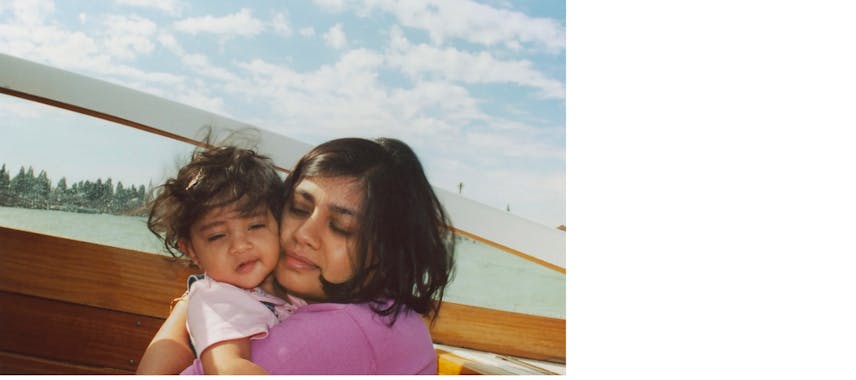 A mother hugging a baby close to her, both with eyes closed, with a city skyline and blue sky in the background.