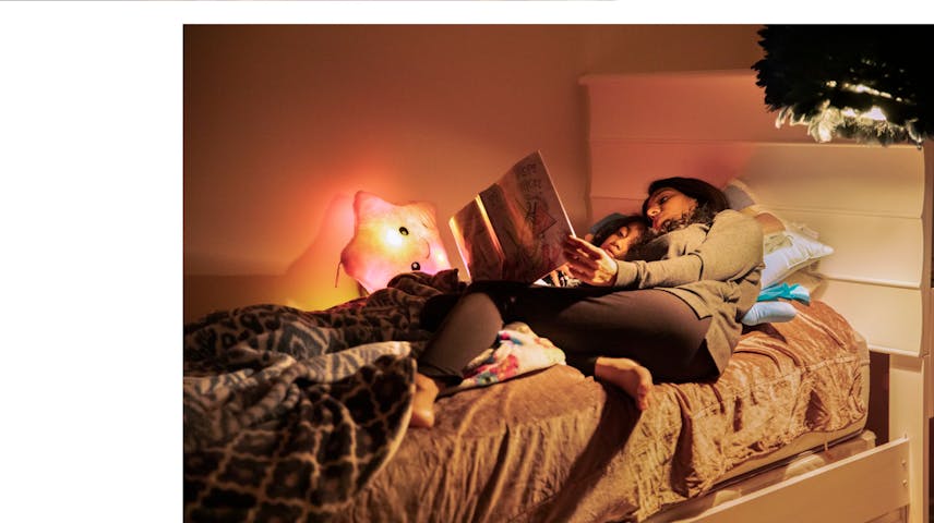 Two related photographs: One is showing a mother hugging a baby close to her and both of them have their eyes closed. In the background is a city skyline and blue sky. The other shows a mother and daughter cuddled in bed while the mother reads a storybook aloud. This photo is dominated by shades of brown.