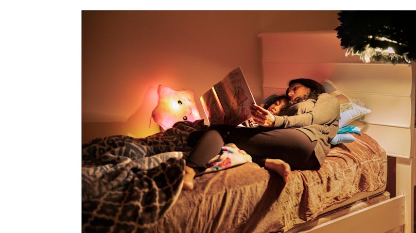 A mother and daughter cuddled in bed while the mother reads a storybook aloud.
