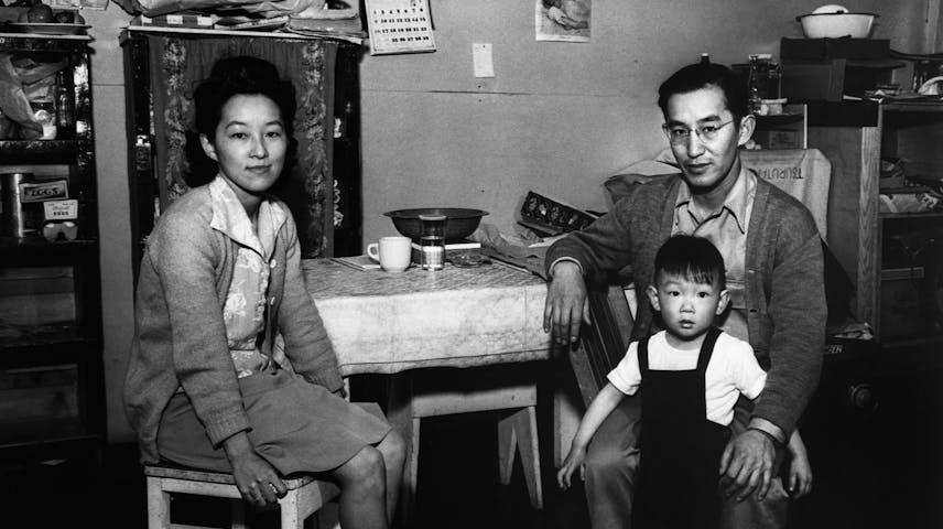Black-and-white photograph of Japanese American adults and child sitting at a table.
