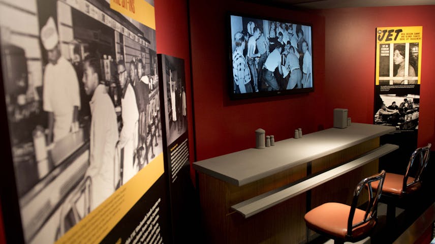 A Newseum Museum exhibit called “The Sit-Ins” about the Civil Rights Movement and showing a section of the original F.W. Woolworth lunch counter from Greensboro, North Carolina, where in 1960 four Black college students launched the sit-in movement. The display includes historical black and white photographs of the sit-in, a reconstructed lunch counter with stools, a video screen showing footage from the era and a cover of Jet magazine featuring “Sit-In Student Freedom Fighters.”