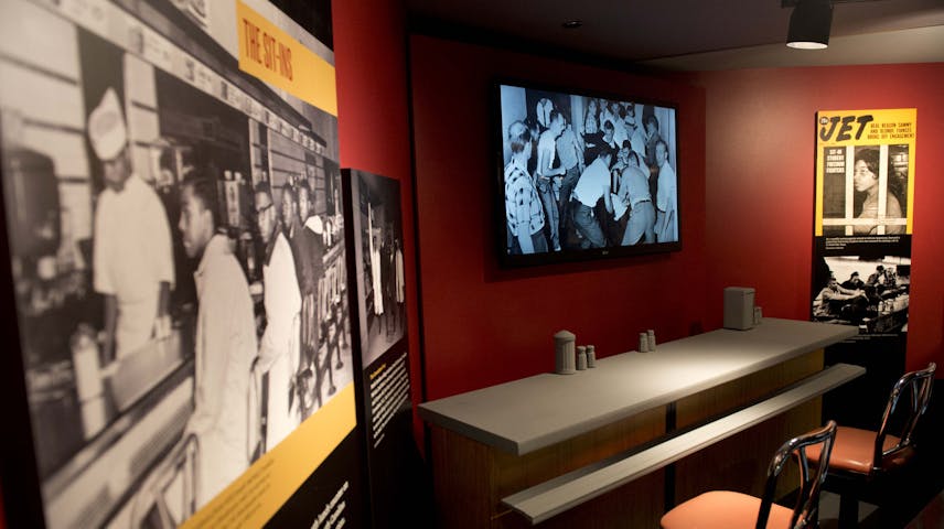 A Newseum Museum exhibit called “The Sit-Ins” about the Civil Rights Movement and showing a section of the original F.W. Woolworth lunch counter from Greensboro, North Carolina, where in 1960 four Black college students launched the sit-in movement. The display includes historical black and white photographs of the sit-in, a reconstructed lunch counter with stools, a video screen showing footage from the era and a cover of Jet magazine featuring “Sit-In Student Freedom Fighters.”