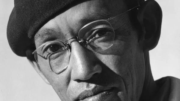 Black-and-white portrait photograph of a Japanese man, Toyo Miyatake, wearing wire-rimmed glasses and a dark beret, looking seriously at the camera. He is wearing a light-colored jacket.