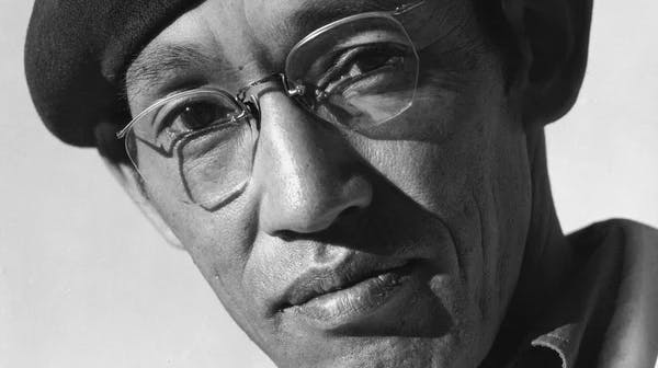 Black-and-white portrait photograph of a Japanese man, Toyo Miyatake, wearing wire-rimmed glasses and a dark beret, looking seriously at the camera. He is wearing a light-colored jacket.