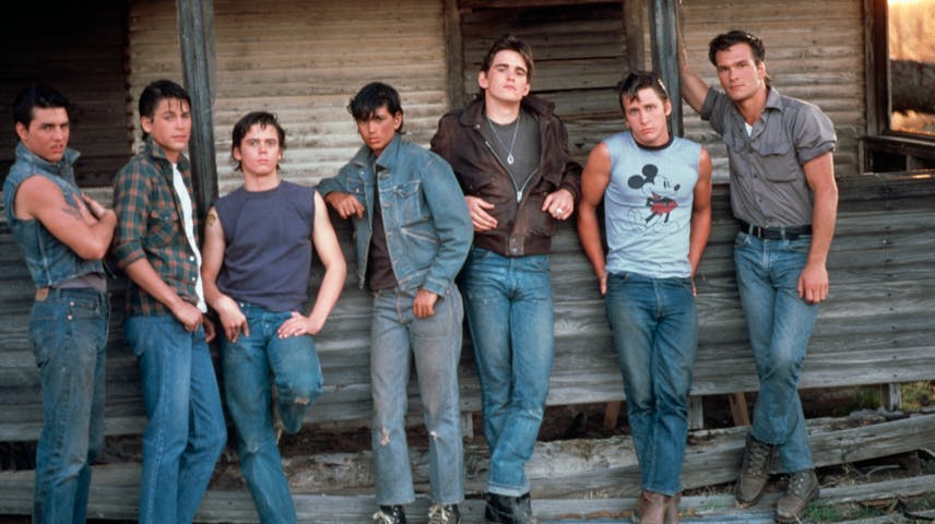 Seven actors (Tom Cruise, Rob Lowe, C. Thomas Howell, Ralph Macchio, Matt Dillon, Emilio Estevez and Patrick Swayze) portray teenage boys in The Outsiders while leaning against the weathered wooden wall of an old building. They wear 1960s-style clothing and hairstyles, including denim jackets, flannel shirts, jeans, sneakers and duckbills and have a tough, cool attitude. One wears a Mickey Mouse t-shirt.